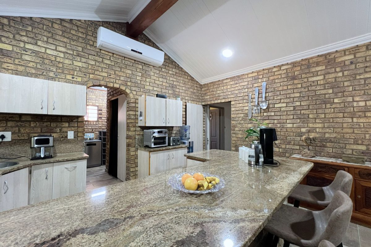 Spacious kitchen featuring exposed brick walls, vaulted ceilings with timber beams, granite countertops, and a large central island with breakfast bar seating.
