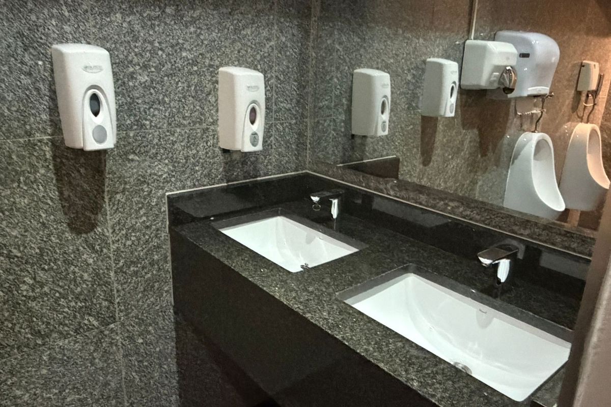 A modern office bathroom featuring a granite vanity with dual undermount sinks, chrome fixtures, and wall-mounted soap dispensers.