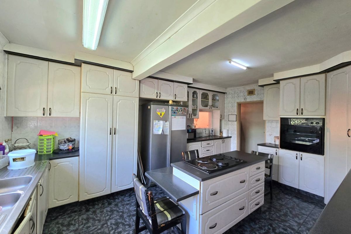 A dated kitchen featuring white cabinetry, a central island with a built-in hob, and dark tiled flooring, offering significant potential for modernization.