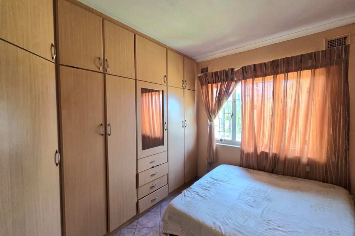 A bedroom featuring extensive built-in wooden cupboards, tiled flooring, and a window with security bars.