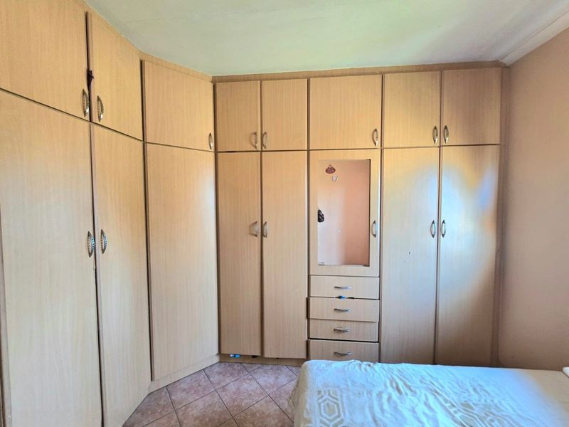 Bedroom featuring extensive light wood-finish built-in cabinetry with integrated storage and vanity mirror, complemented by tiled flooring.