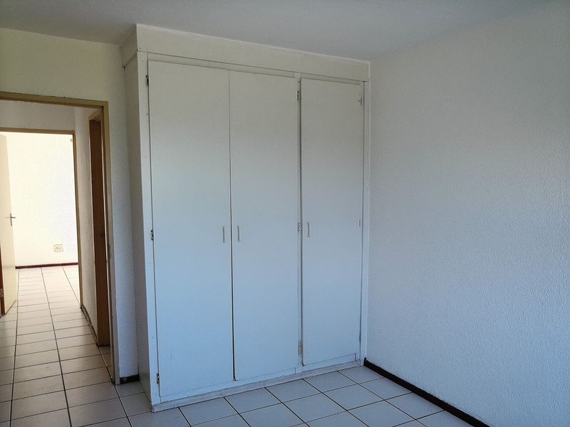 A bedroom featuring built-in cupboards with white doors and tiled flooring, leading into a hallway.