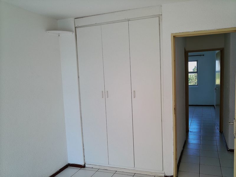 A bedroom interior featuring built-in white cupboards and tiled flooring, with a doorway leading to an adjacent room.