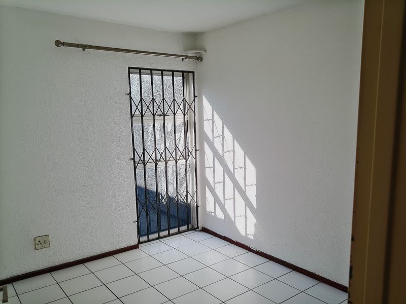 An empty room featuring white textured walls, tiled flooring, and a security gate over the doorway.