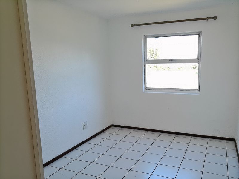 A clean, empty bedroom featuring white walls, tiled flooring, and a single window with a curtain rod.