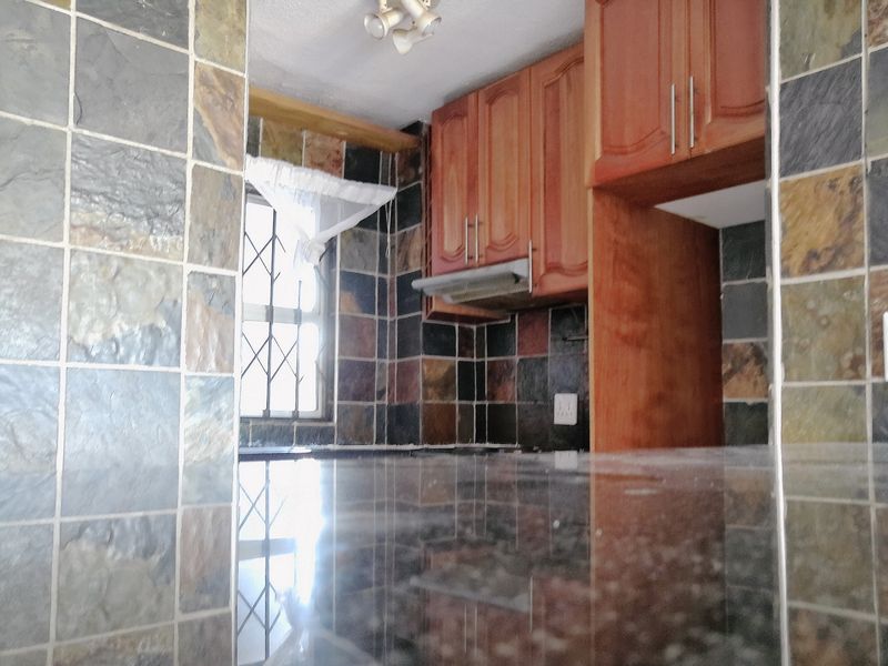 A kitchen featuring dark stone-look wall tiles, wooden cabinetry, and a polished countertop, offering a functional workspace with natural light.