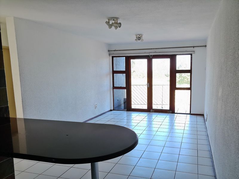 An open-plan living area featuring tiled flooring, a breakfast bar counter, and double glass doors leading to an outdoor balcony space.