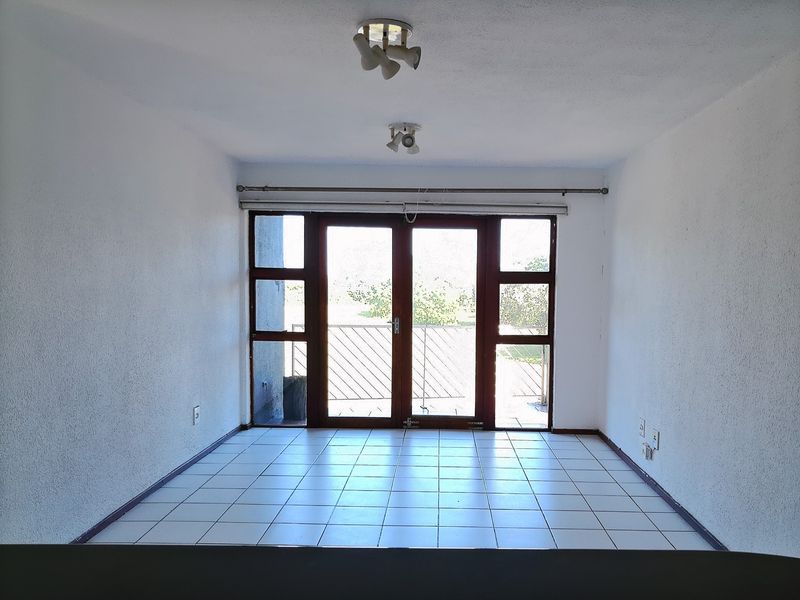 An empty living area featuring tiled flooring, dual ceiling light fixtures, and large glass doors providing access to an outdoor balcony.