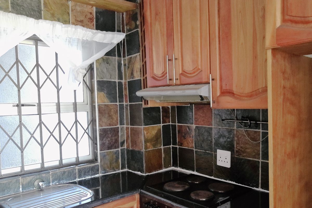 A functional kitchen area featuring wooden cabinetry, a built-in hob with extractor fan, and a dark stone countertop with a stainless steel sink.