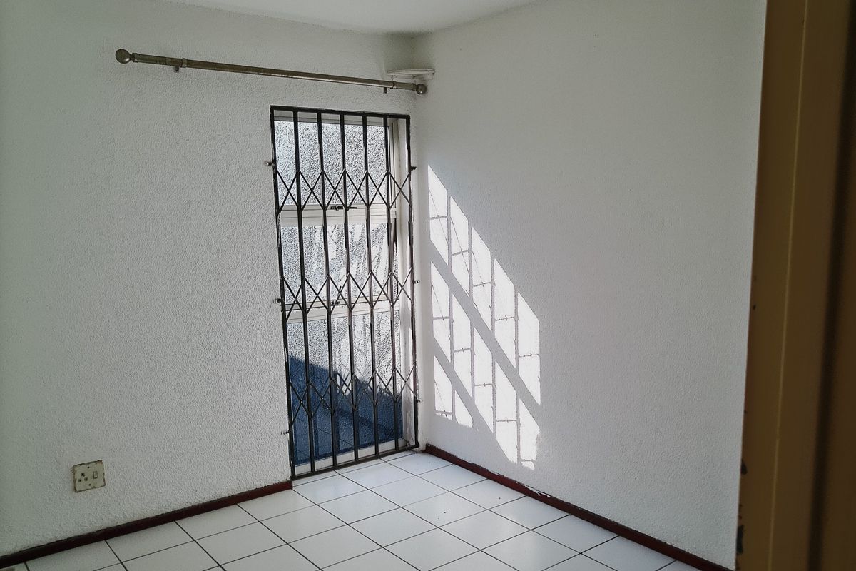 An empty room featuring white textured walls, tiled flooring, and a security gate over the doorway.