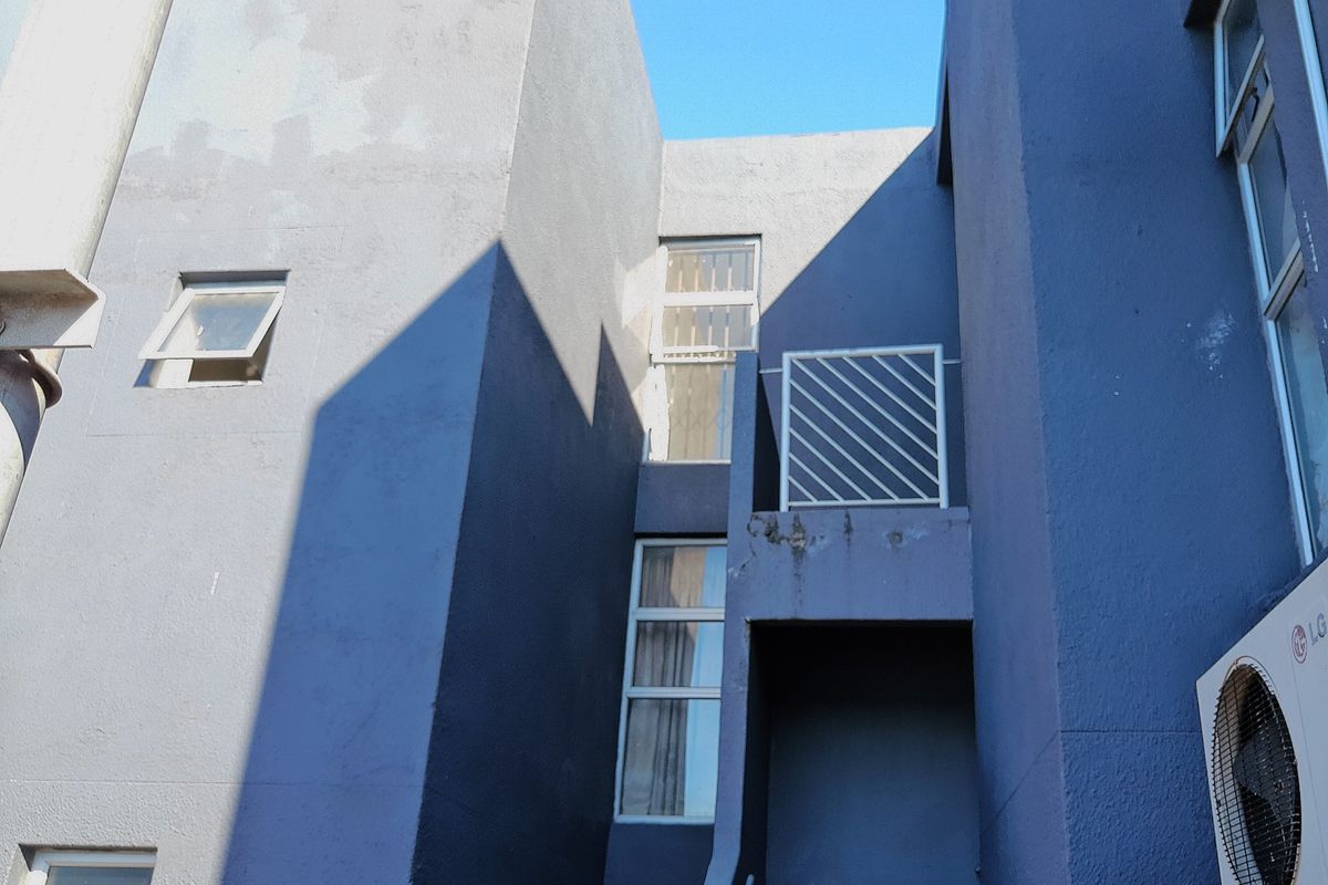 Exterior view of a multi-story residential building featuring textured blue facade, metal security bars, and integrated air conditioning unit.