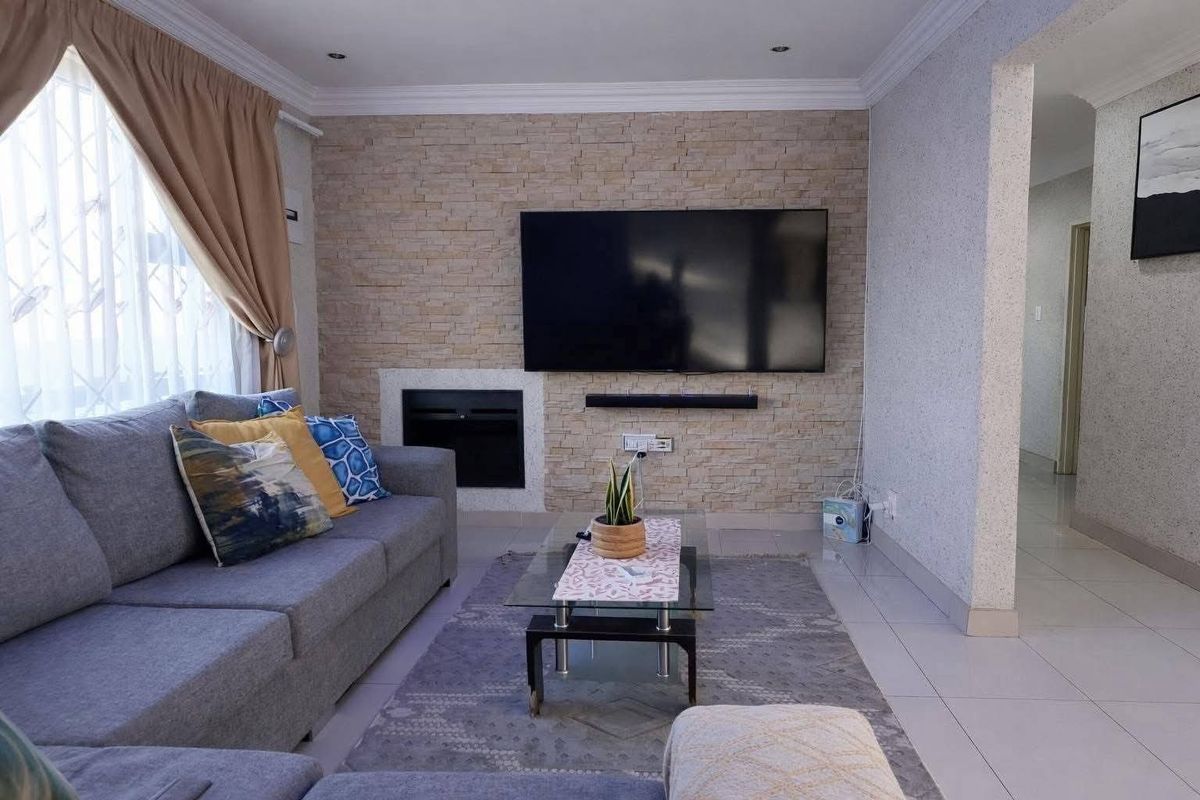 A well-maintained living room featuring a textured stone accent wall with a built-in fireplace and modern tiled flooring.
