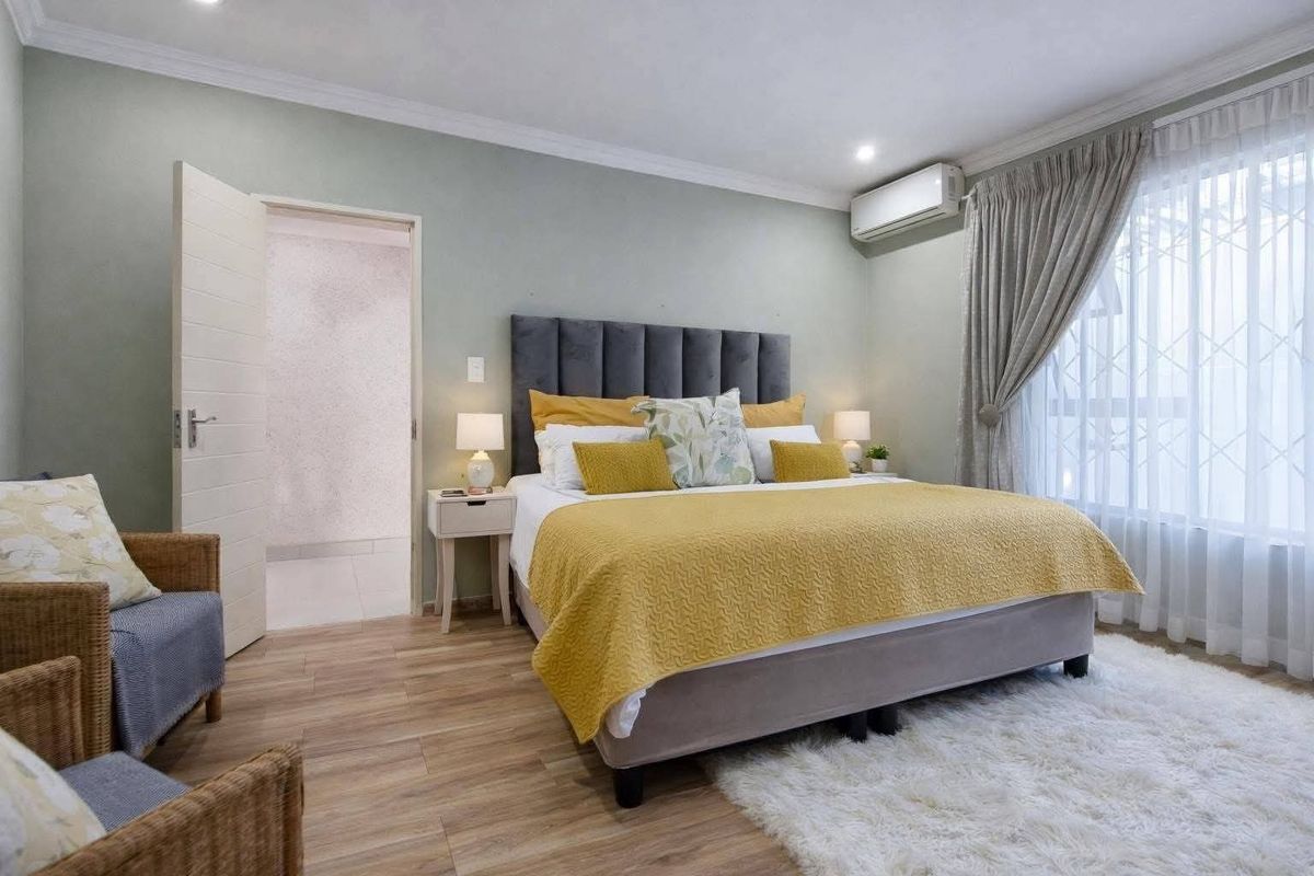 A well-maintained bedroom featuring laminate flooring, coved ceilings, and a wall-mounted air conditioning unit, with an adjoining doorway leading to an ensuite.