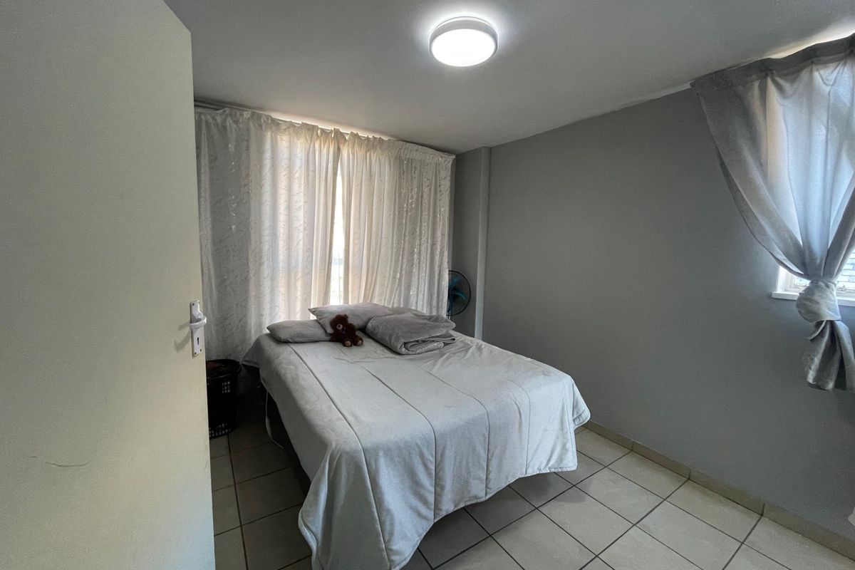 A functional bedroom featuring neutral wall tones, tiled flooring, and a central flush mount light fixture.