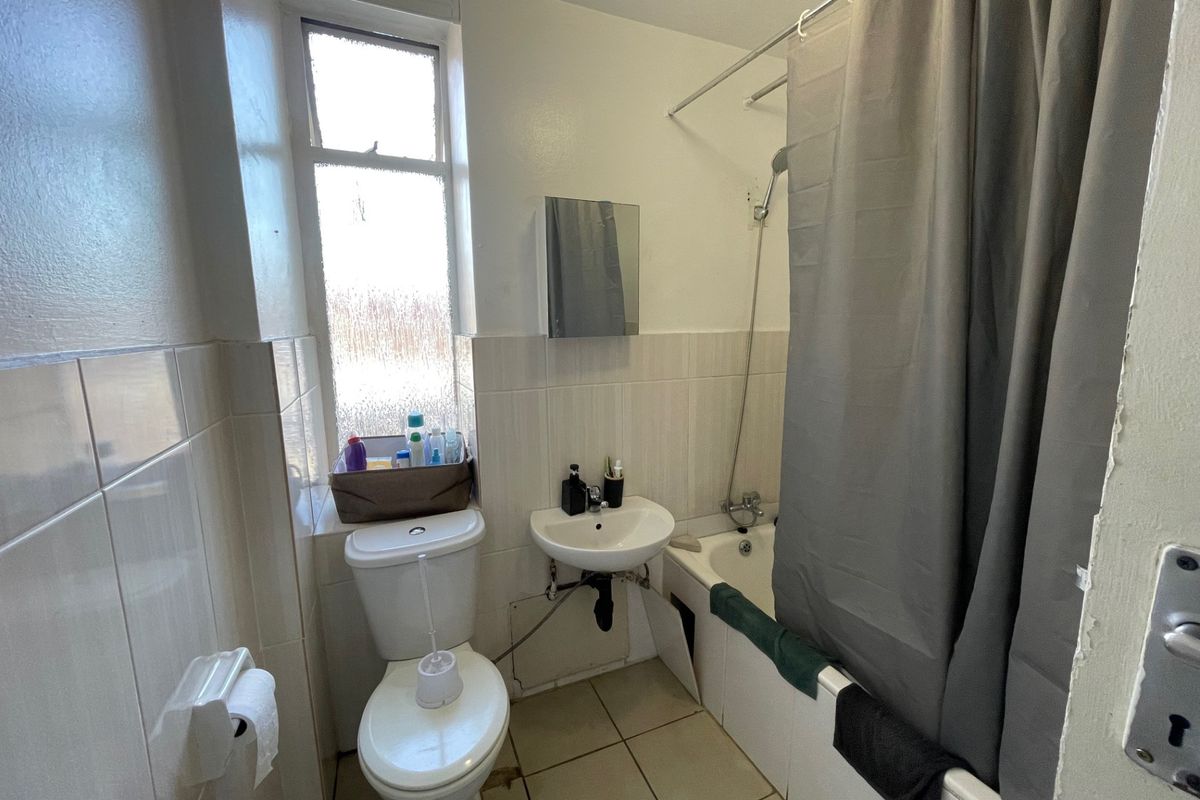 Compact bathroom featuring a bathtub with shower attachment, pedestal sink, and toilet, finished with neutral wall and floor tiles.