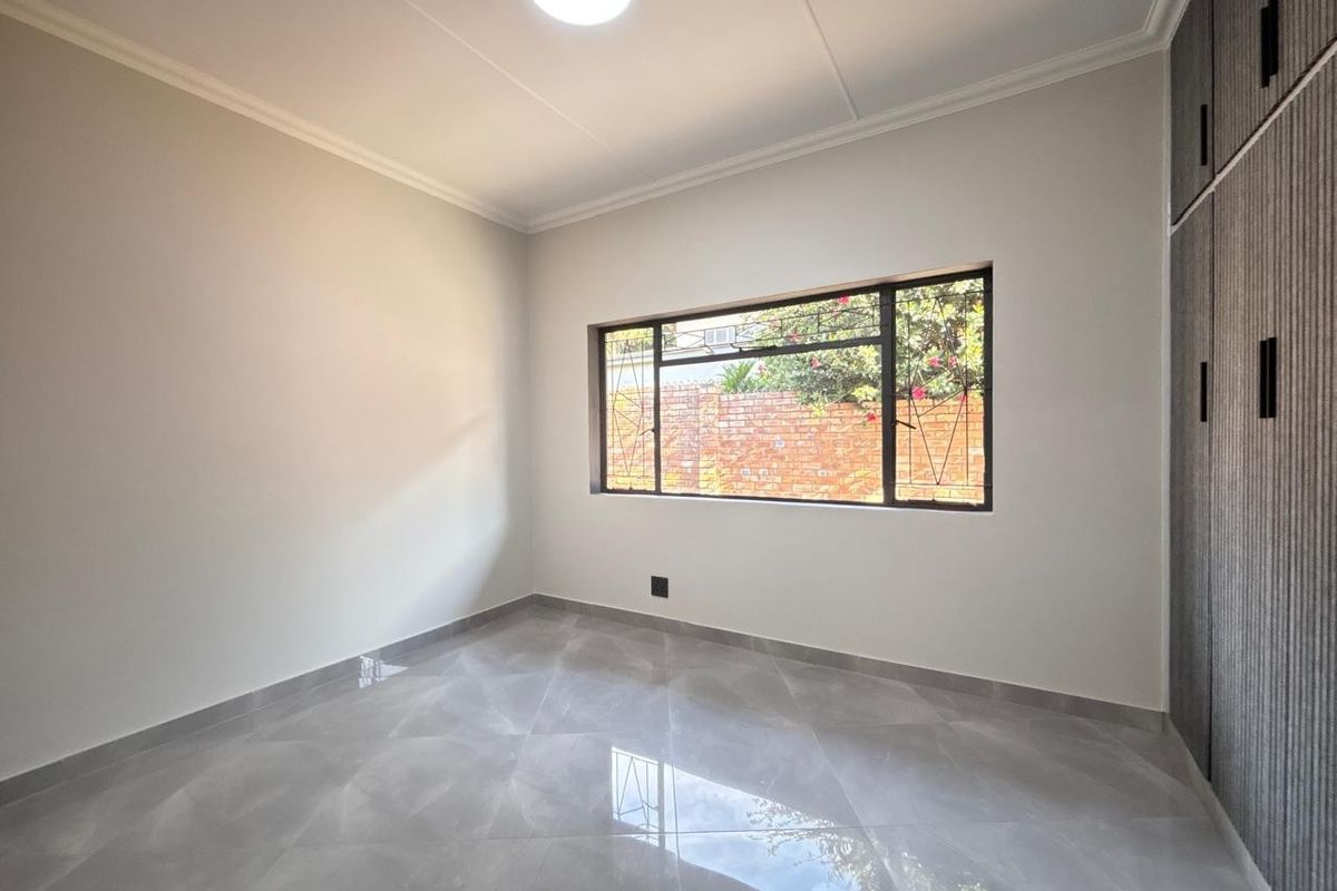 A bright, empty bedroom featuring modern grey floor tiles, neutral walls, and built-in floor-to-ceiling cupboards.
