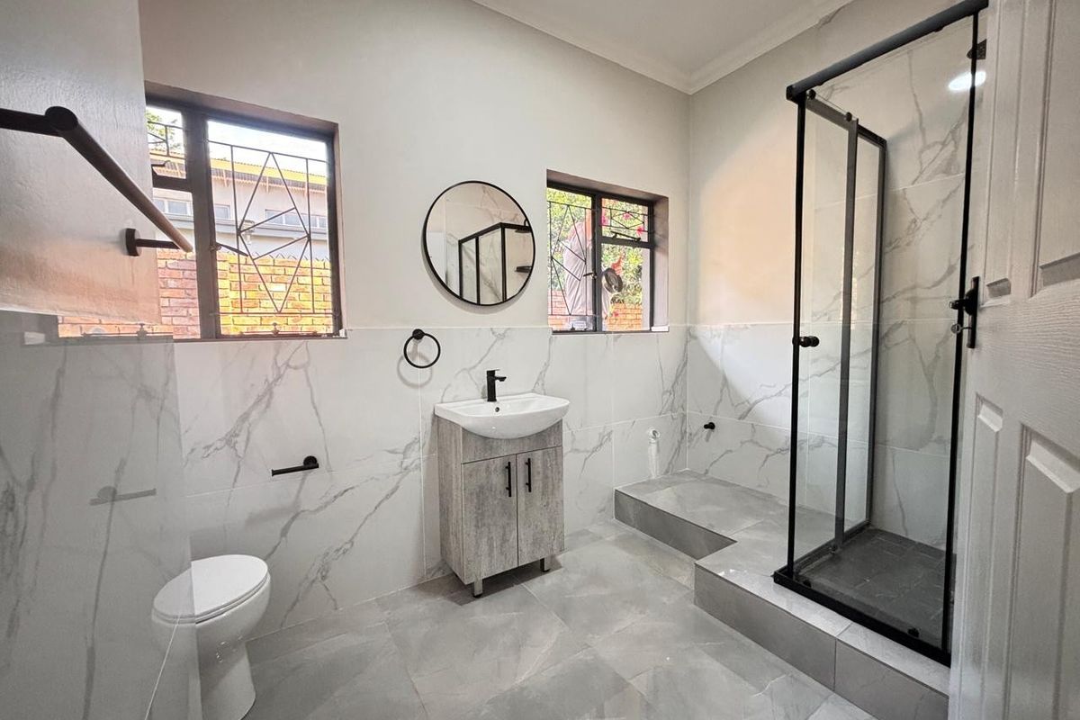 Modern bathroom featuring a walk-in shower with black frame, marble-look wall tiles, grey floor tiles, and a contemporary vanity unit.