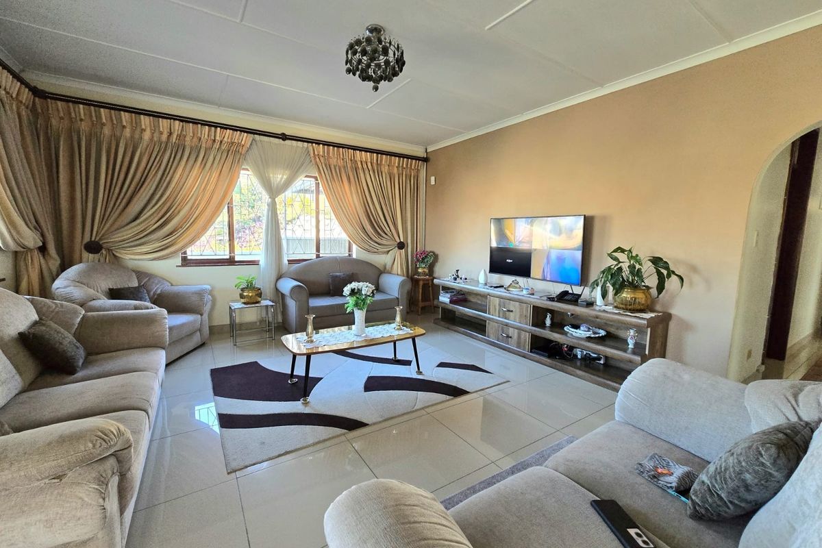 A spacious living room featuring polished tiled flooring, neutral wall tones, and large windows dressed with heavy curtains.