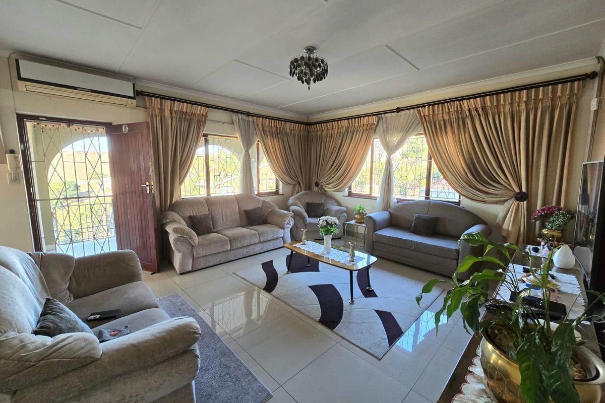 A spacious living room featuring tiled flooring, a wall-mounted air conditioning unit, and large windows with curtain rails, providing a bright and functional living space.