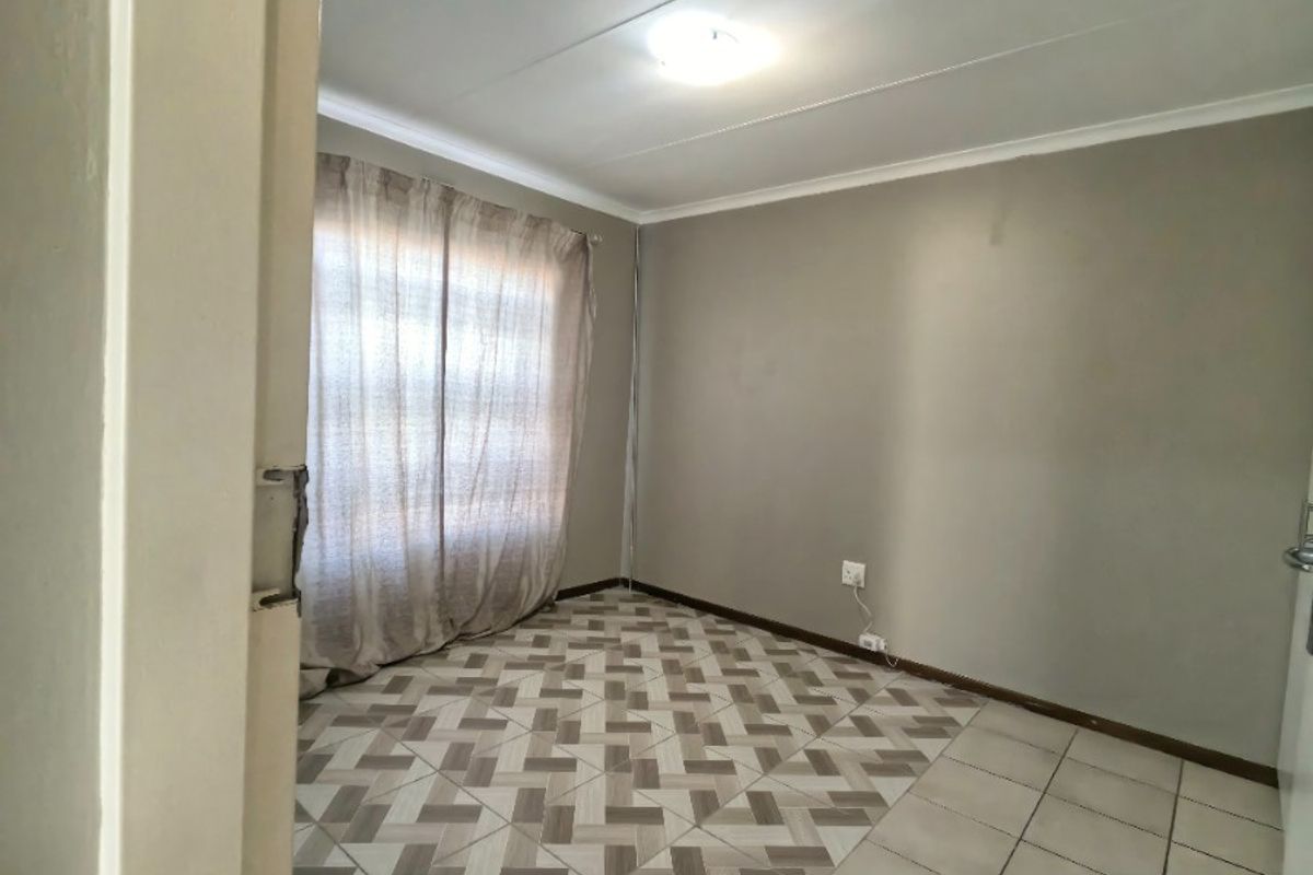 A vacant bedroom featuring a mix of patterned and plain ceramic floor tiles, neutral wall paint, and a standard ceiling light fixture.
