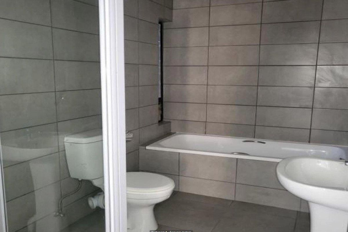 A modern bathroom featuring grey wall tiles, a built-in bathtub, a pedestal sink, and a separate glass-enclosed shower area.