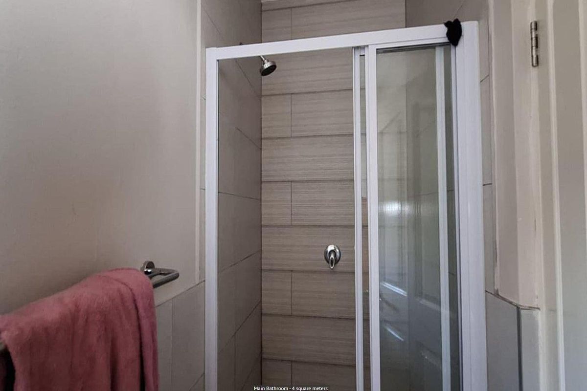 A modern bathroom shower enclosure featuring neutral-toned wall tiles, a glass sliding door, and a chrome shower mixer.