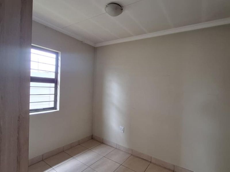 A simple, empty bedroom featuring tiled flooring, a window with security bars, and a built-in wardrobe.