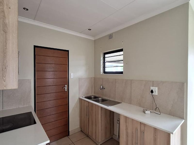 A functional kitchen featuring light wood-grain cabinetry, stone-look countertops, a built-in electric hob, and a double stainless steel sink.