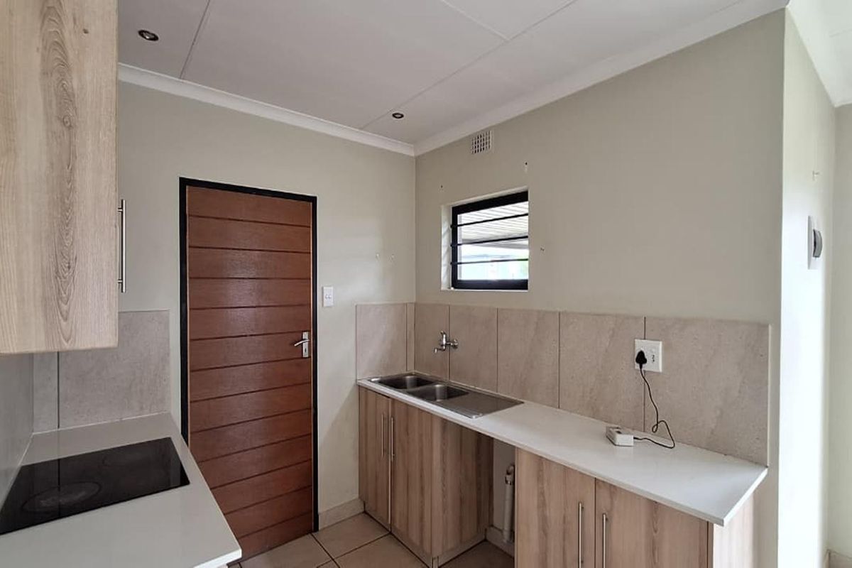 A functional kitchen featuring light wood-grain cabinetry, stone-look countertops, a built-in electric hob, and a double stainless steel sink.