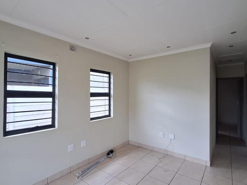 A bright, empty living room featuring neutral tiled flooring, recessed ceiling lighting, and security bars on the windows.