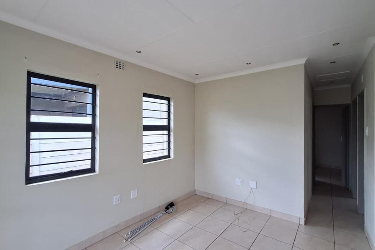 A bright, empty living room featuring neutral tiled flooring, recessed ceiling lighting, and security bars on the windows.