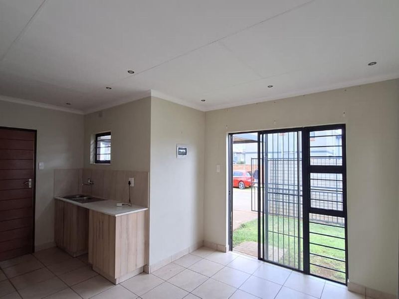 An open-plan living area featuring tiled flooring, a compact kitchenette with built-in cabinetry, and sliding glass doors leading to the exterior.