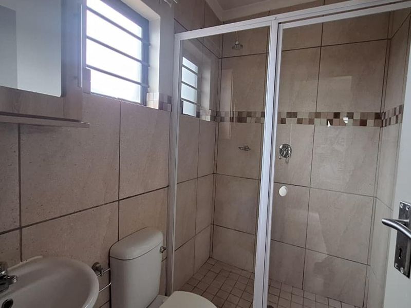 A functional bathroom featuring a glass-enclosed shower, tiled walls, a pedestal basin, and a toilet.