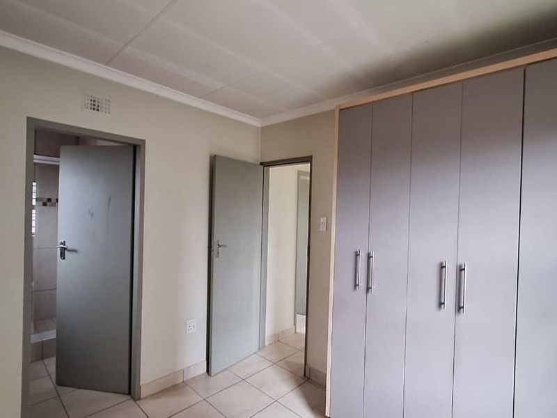 A bedroom featuring built-in cupboards with grey doors and tiled flooring, providing direct access to an en-suite bathroom.