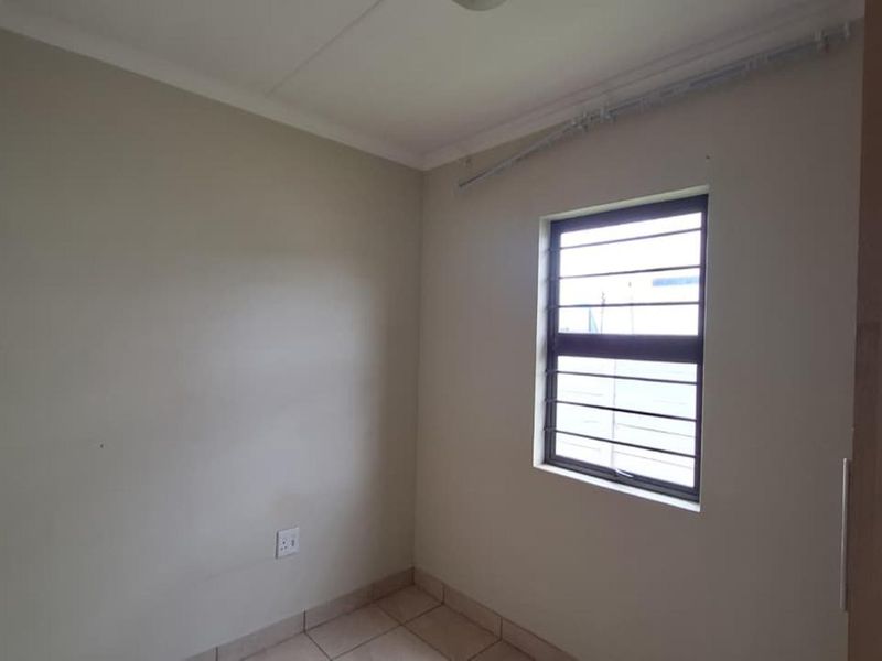 A compact, empty bedroom featuring tiled flooring, a window with security bars, and neutral wall finishes.