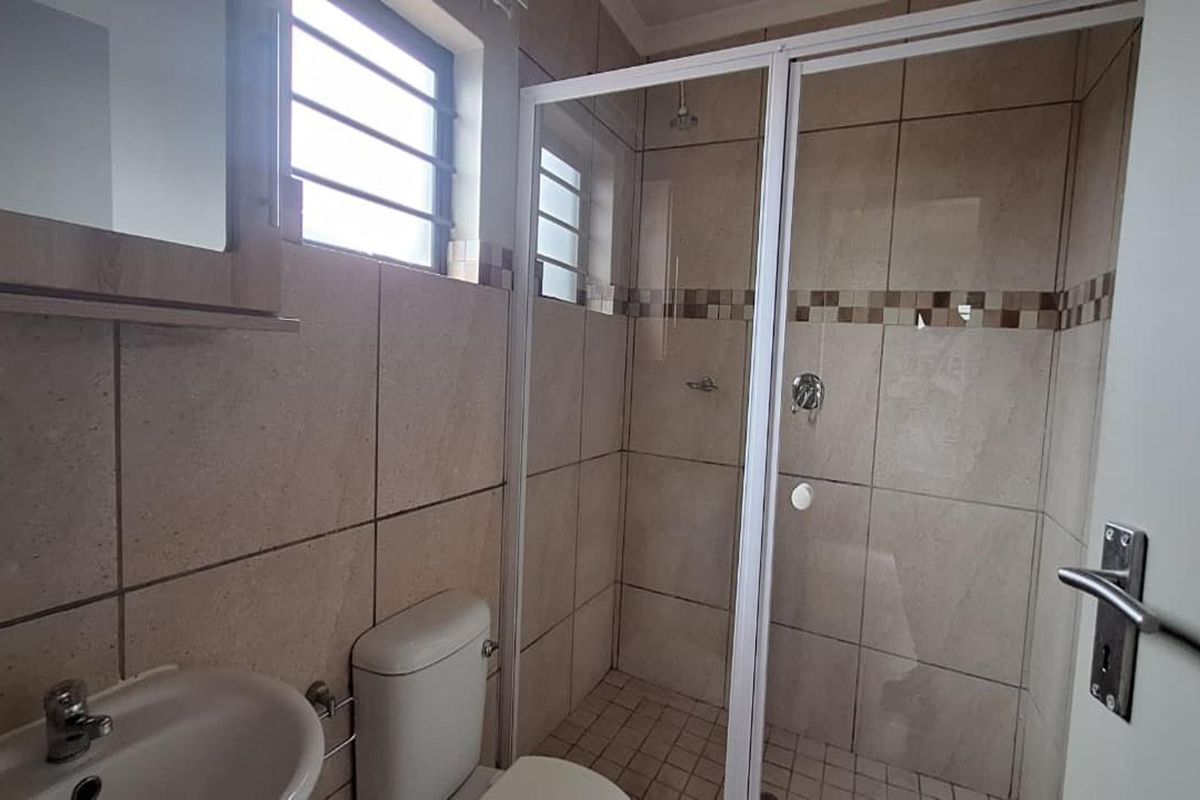 A functional bathroom featuring a glass-enclosed shower, tiled walls, a pedestal basin, and a toilet.
