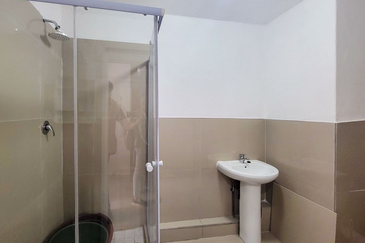 A functional bathroom featuring a glass-enclosed shower stall and a white pedestal sink with neutral wall tiling.