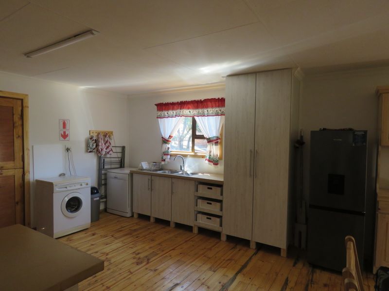 A functional kitchen area featuring light-toned cabinetry, a stainless steel sink, and integrated laundry appliance space with exposed timber flooring.