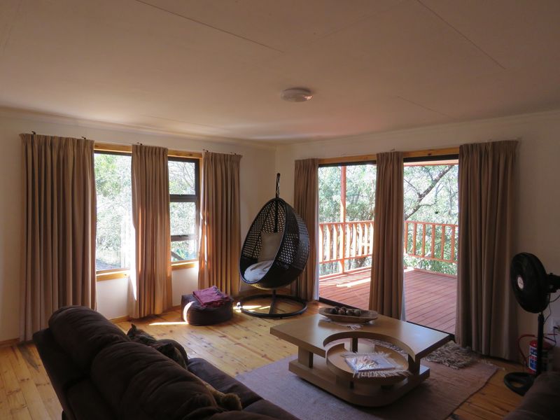 A bright living room featuring polished timber flooring, large windows, and sliding glass doors that open onto an elevated wooden deck.