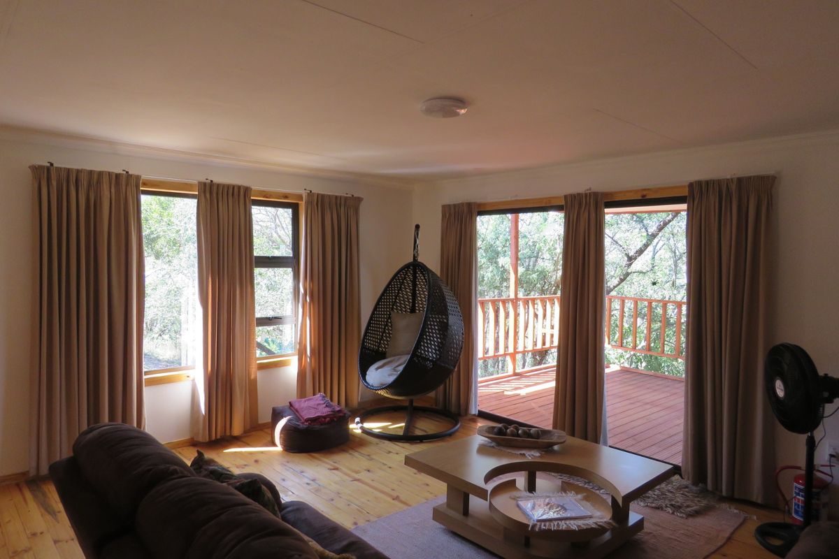 A bright living room featuring polished timber flooring, large windows, and sliding glass doors that open onto an elevated wooden deck.