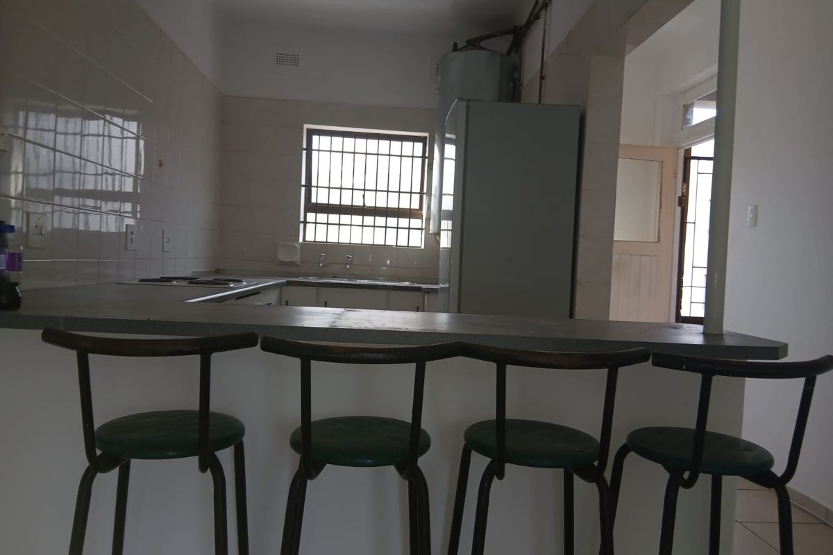 A dated kitchen featuring a breakfast bar, tiled splashbacks, and exposed plumbing, offering potential for a modern renovation.