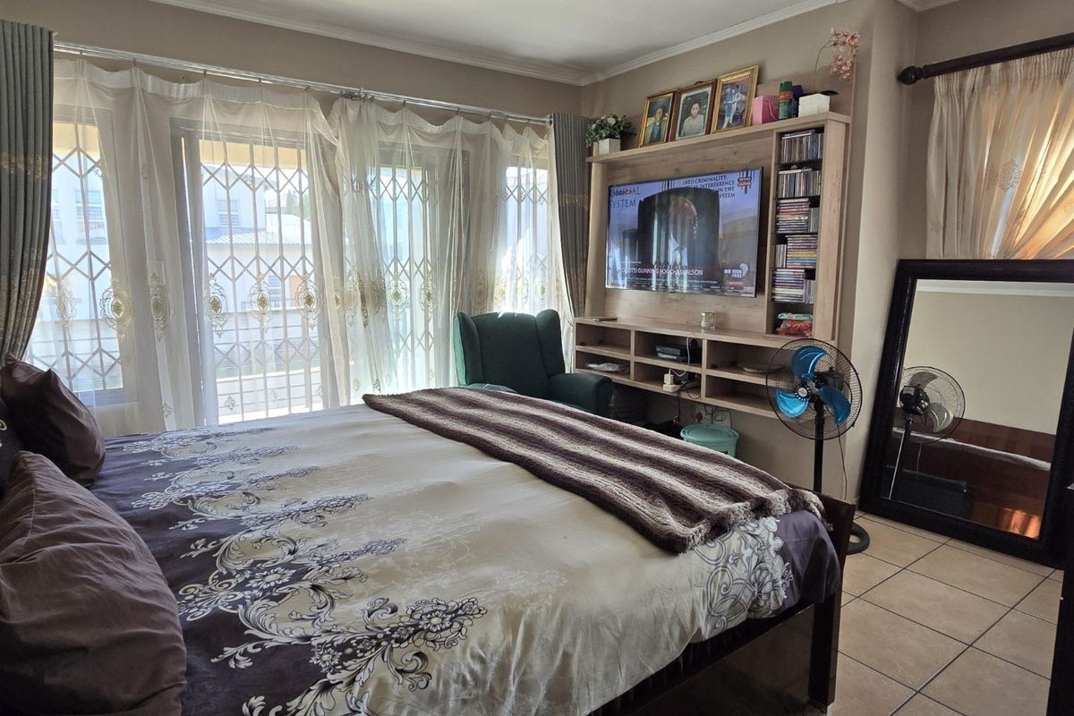 A well-lit bedroom featuring tiled flooring, built-in shelving unit, and large sliding glass doors with security gates leading to an outdoor area.