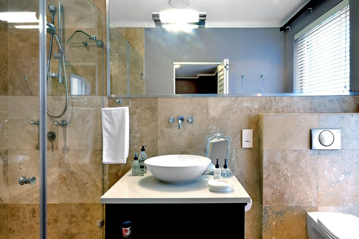 Modern bathroom featuring a stone-tiled walk-in shower, a contemporary vessel sink vanity, a large wall-mounted mirror, and a wall-hung toilet.