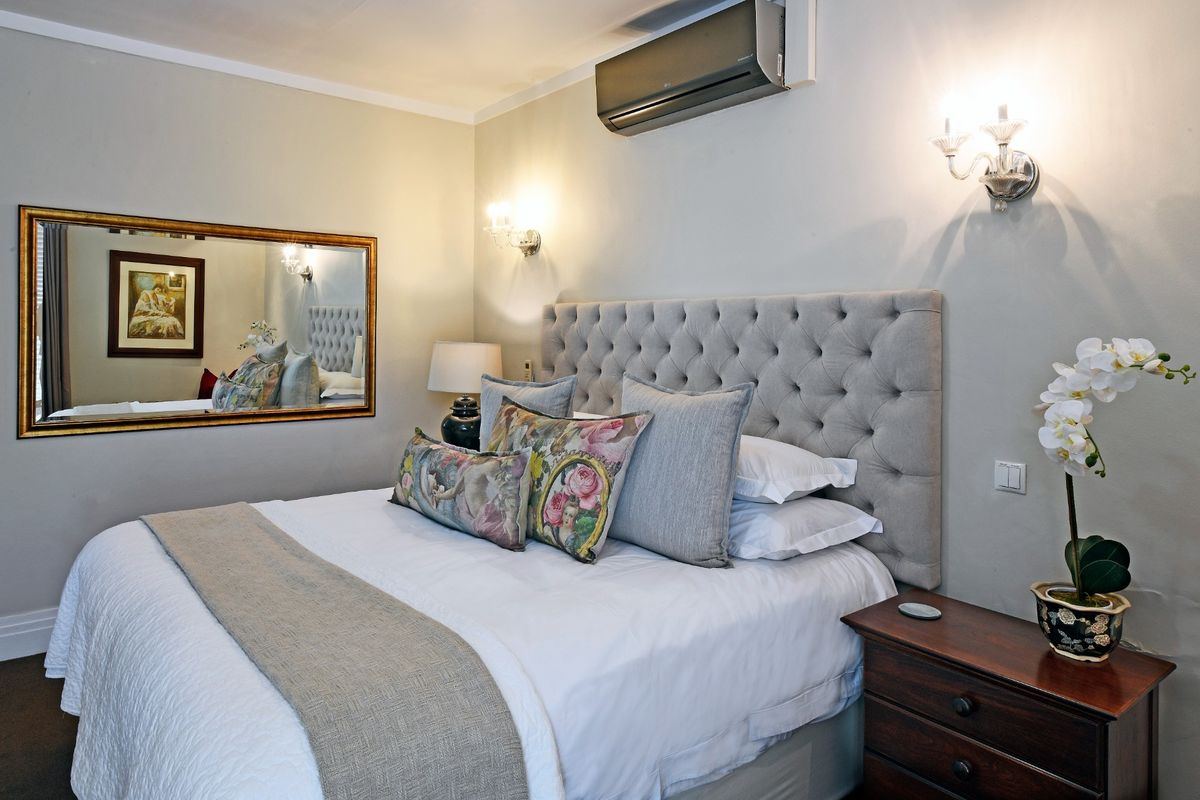 A well-appointed bedroom featuring a tufted headboard, wall-mounted air conditioning unit, and decorative wall sconces.