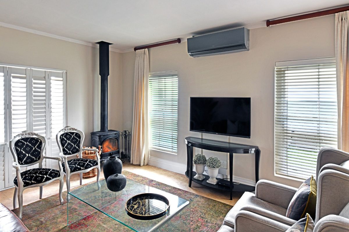 A well-maintained living room featuring a built-in wood-burning fireplace, wall-mounted air conditioning unit, and large windows with fitted blinds.
