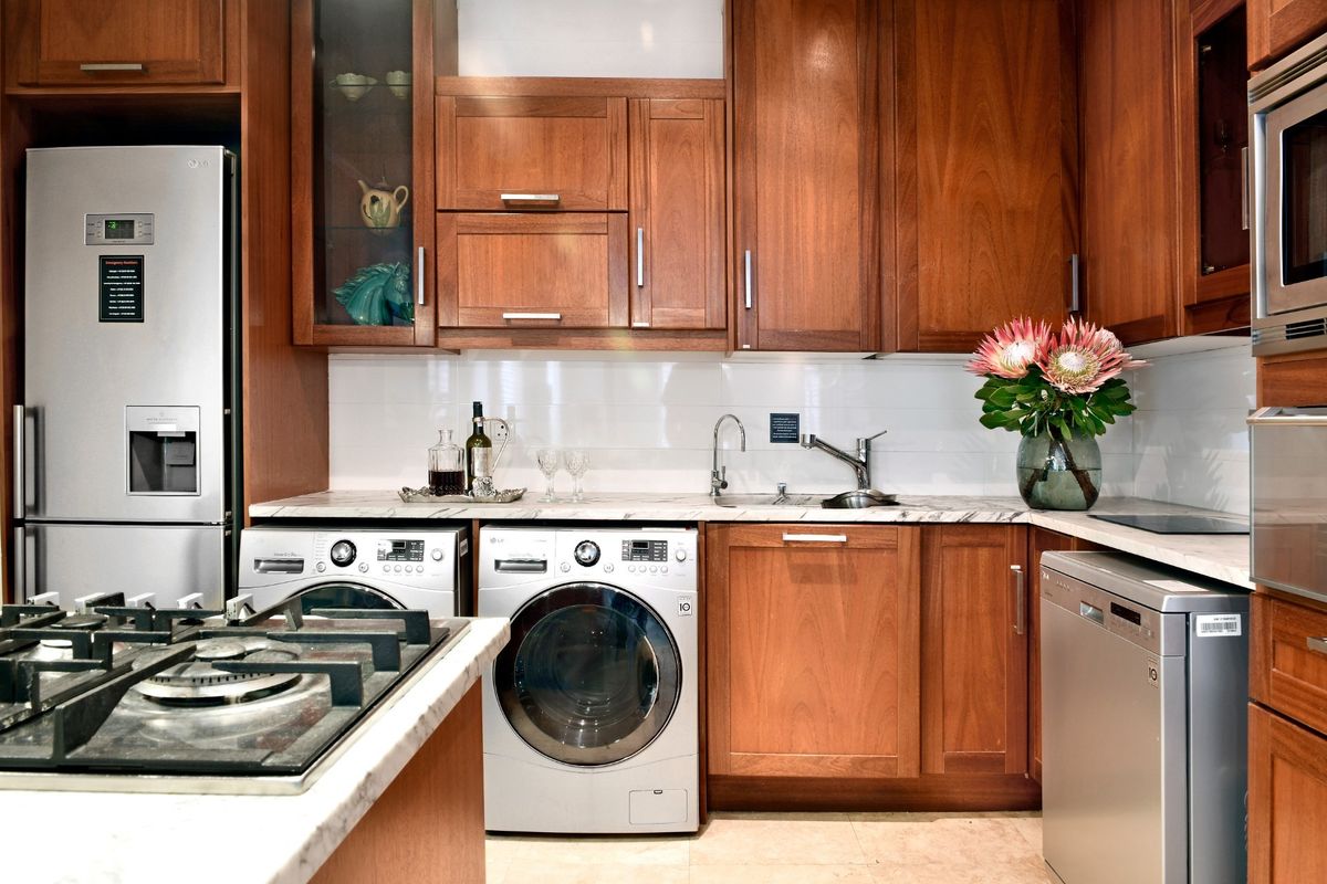 A well-appointed kitchen featuring warm wood cabinetry, stone countertops, integrated stainless steel appliances, and a dedicated laundry area with built-in washing machine.