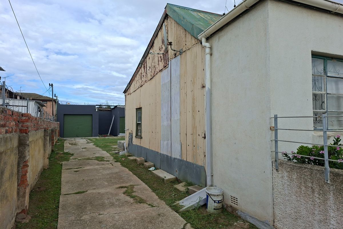 Side view of the property showing a concrete driveway, boundary wall, and exterior wall cladding in need of maintenance and repair.