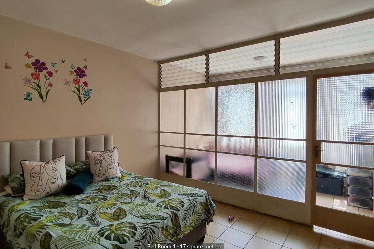 Spacious bedroom featuring tiled flooring and a large glass partition wall with integrated door providing access to an adjoining area.