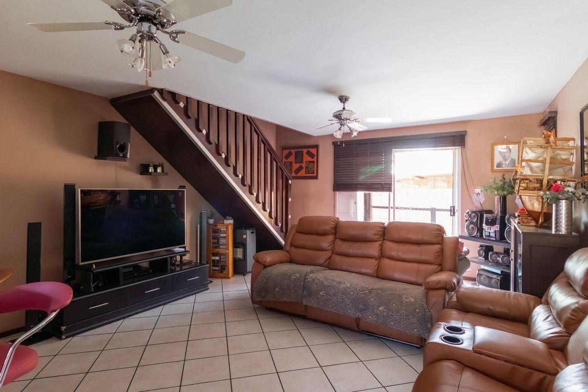 Spacious living room featuring tiled flooring, a built-in staircase with wooden balustrades, and sliding glass doors providing access to the outdoor area.