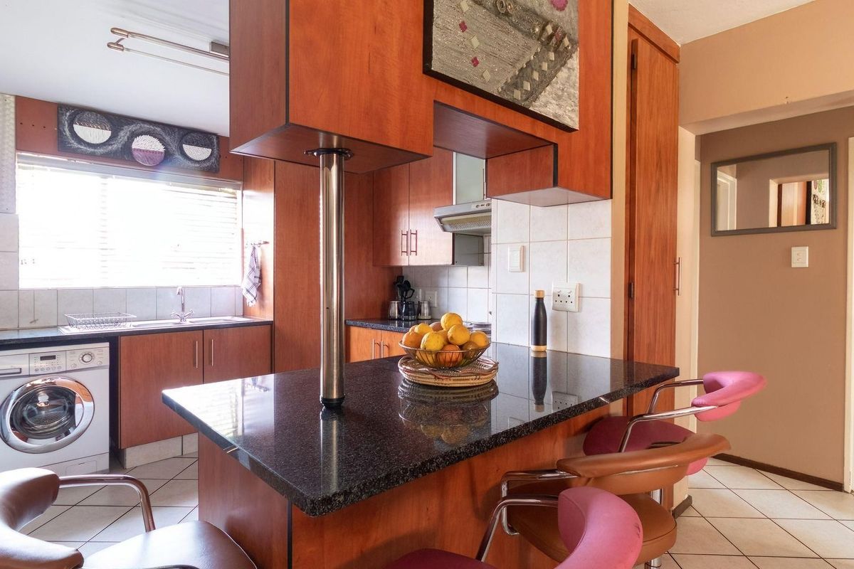 A functional kitchen featuring wood-finish cabinetry, a dark granite breakfast bar, tiled flooring, and an integrated laundry area.